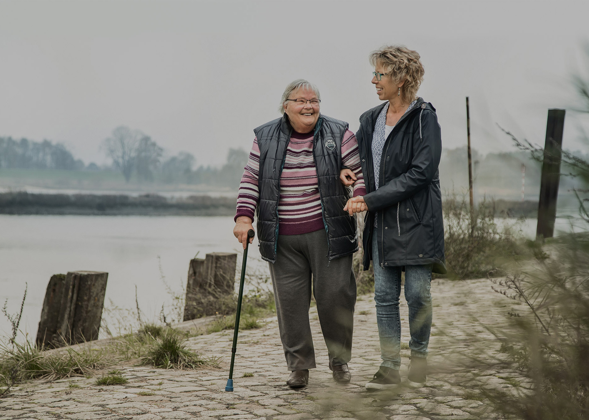 Frau spaziert mit ihrer Pflegerin an der Elbe entlang